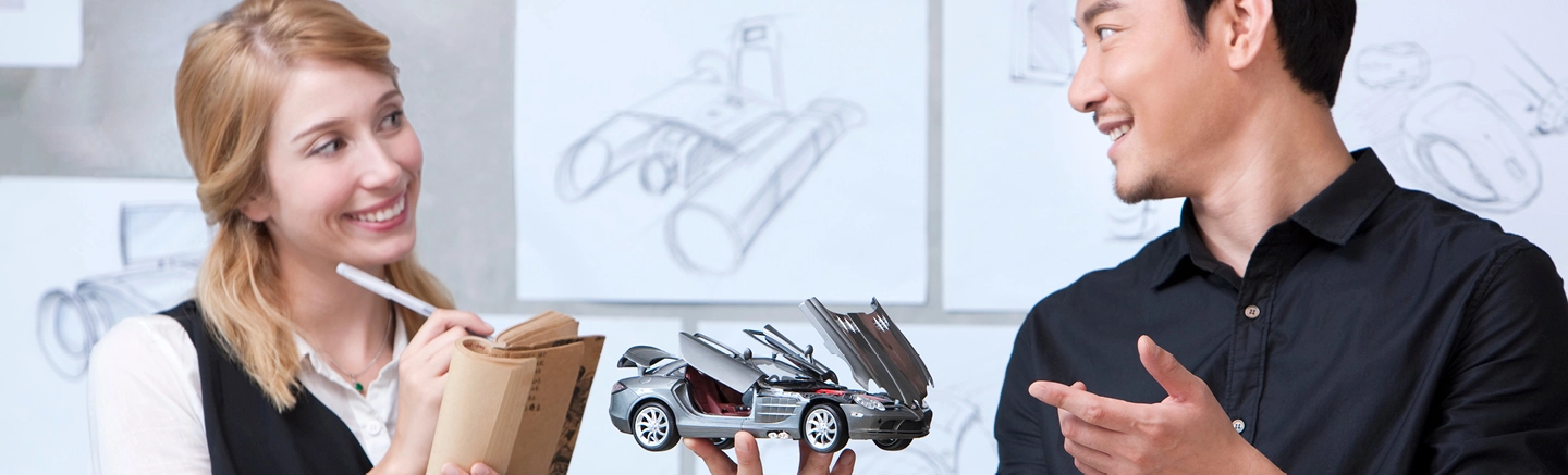 Man and woman smiling and holding a model car